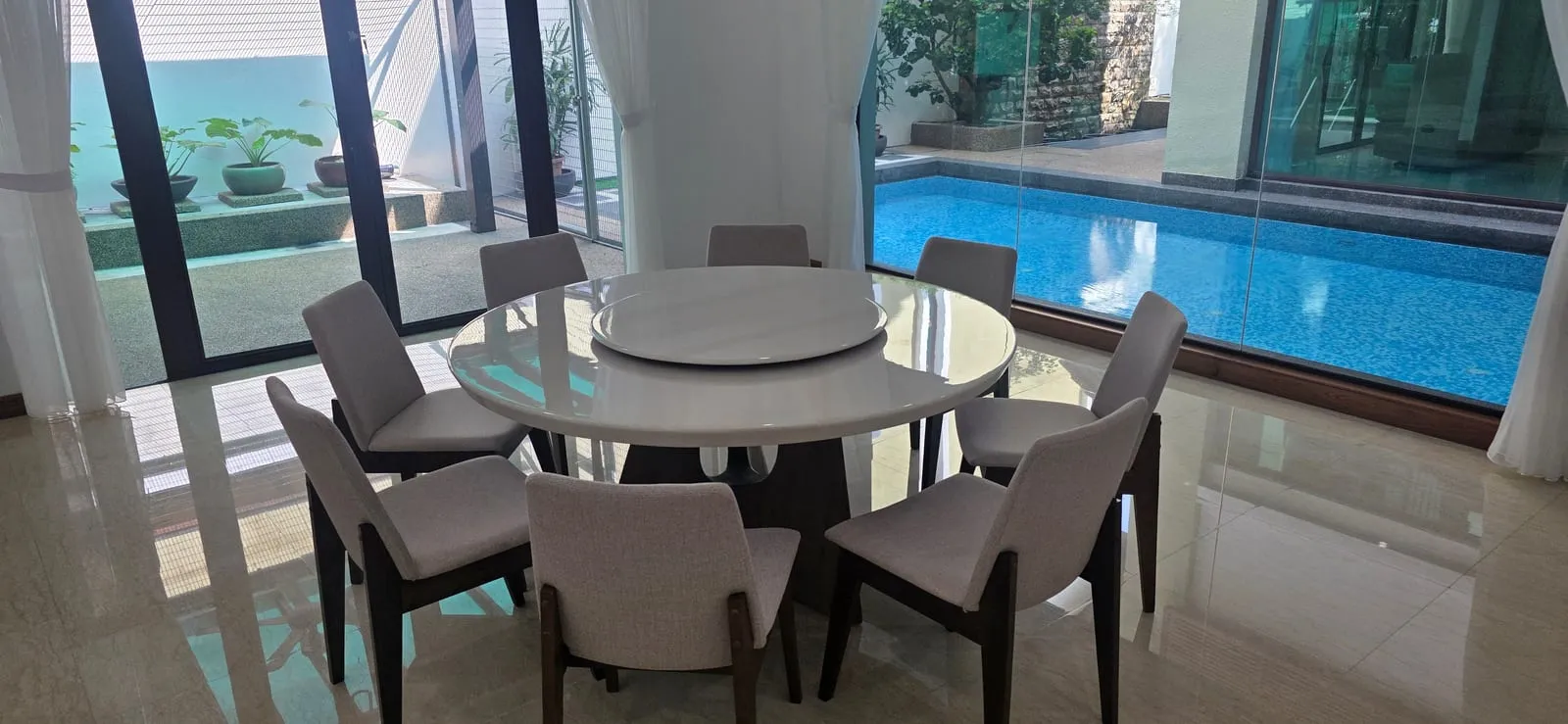 The furnished dining area at Villa Mont Kiara — a round marble dining table for eight between the pool and the courtyard.